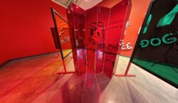 A close-up view of Sora’s red folding screen and plexiglass panels reveals black line drawings of a crying baby Sora in a traditional hanbok, with reflections and overlapping shapes tinting the gallery in red and green hues.