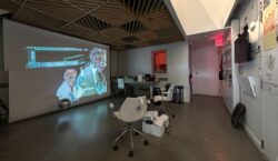 A darker space allows for a large projection against one wall and a discoball hangs suspended from the ceiling, casting bright dots across the containing walls.