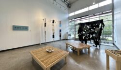 The front entrance and wall of windows is obscured by a hanging mural work made of jeans, with other works from the busy HOHOL group show installed on the floor and west wall.