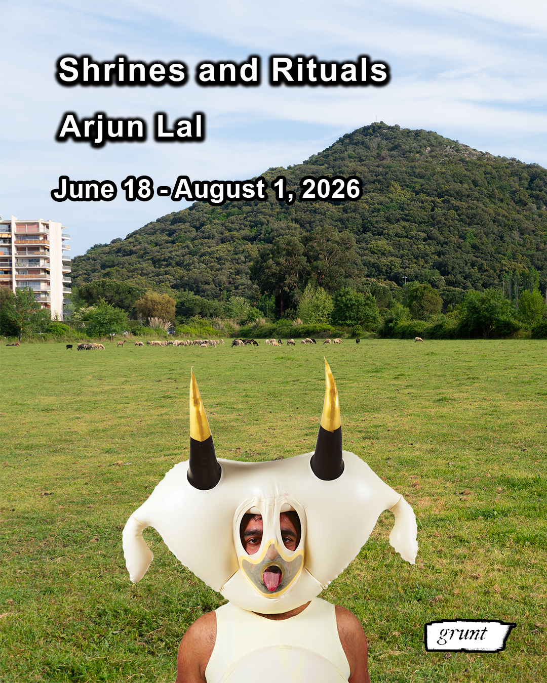 A composite image comprised of Arjun Lal wearing an inflated latex cow costume in front of a green grass field filled with sheep. In the far distance is a bright blue sky with white clouds over a mountain filled with lush foliage and a white, blue, and red apartment building at left. Arjun’s upper body is in frame and they have a neutral face expression as they stick their tongue out. Arjun’s face is partially discernable at the centre of a large headpiece with two large eye holes and a semi-sheer clear latex used that alludes to the lower half of their face. They have dark hair and brown skin. The costume is primarily made of white latex with two long black, gold capped horns at top and an ear at either side of the head. The white latex body piece is like a tank top with a high scoop neckline, Arjun’s shoulders are exposed. Bold white sans-serif text outlined in black reads, “Shrines and Rituals, Arjun Lal, June 18 to August 1, 2026. grunt gallery’s logo appears in white at bottom right.]